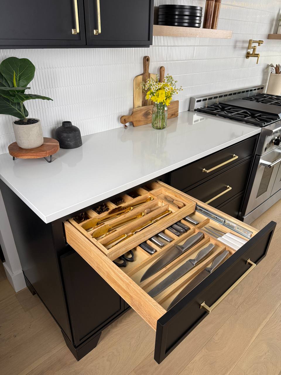 Open knife cutlery drawer in a modern kitchen with white countertops and black cabinets.