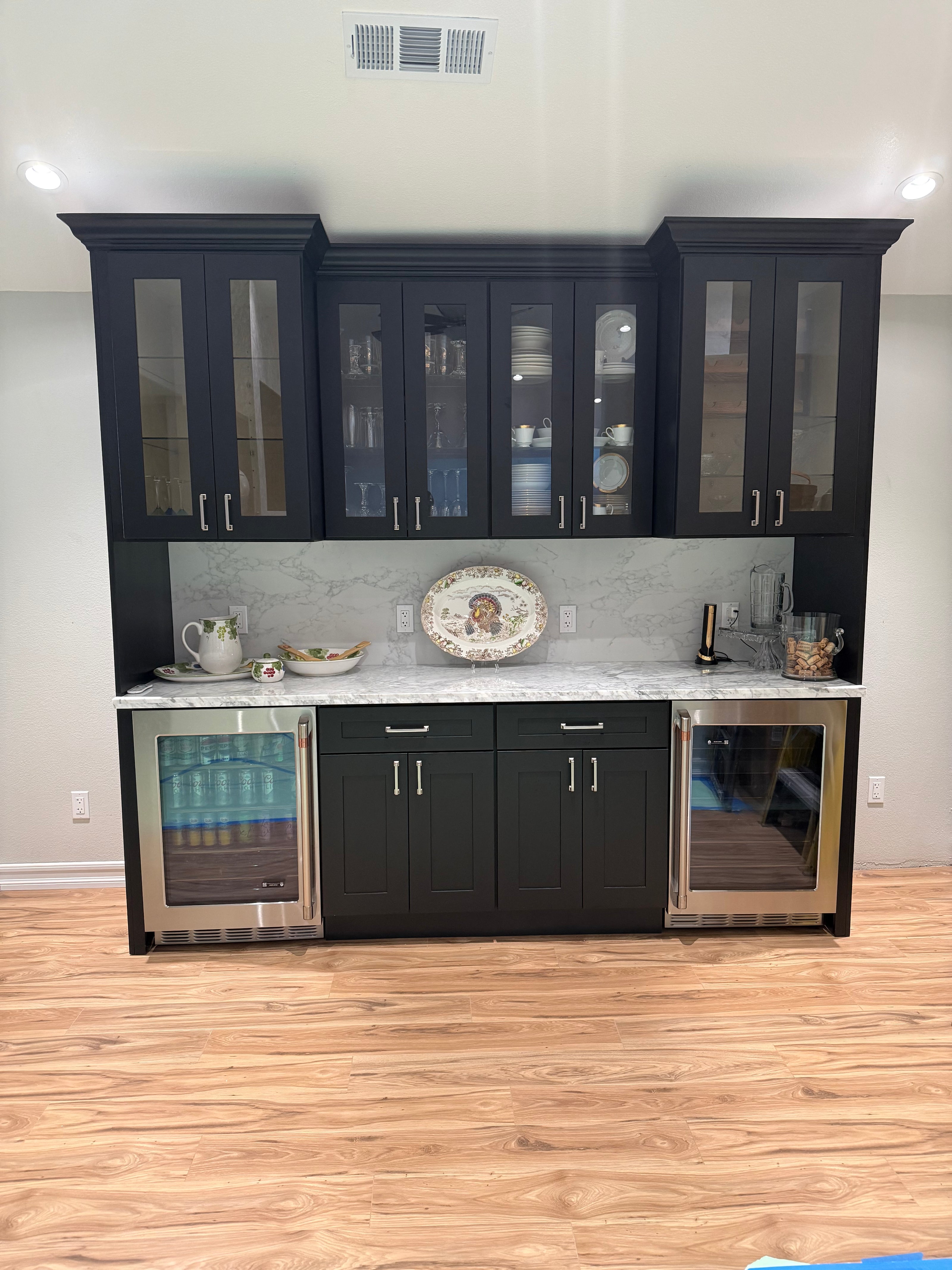 Modern kitchen cabinet with glass doors and metallic handles on a wooden floor.